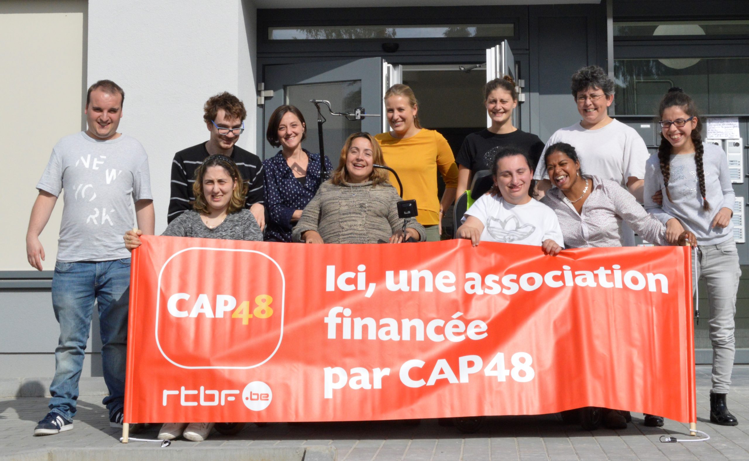 Groupe de bénéficiaires portant une banderole avec comme message : "Ici, une associations financée par CAP48"