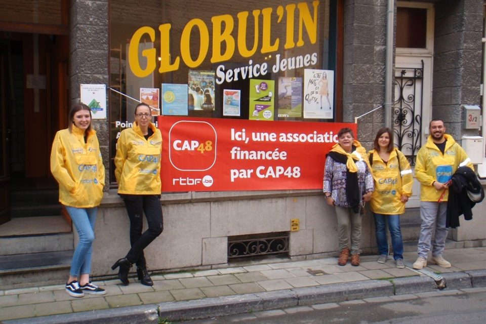 Bénévoles posant devant l'entrée de Globul'in, service d'aide au jeunes en milieu ouvert (AMO), une asbl financée par CAP48