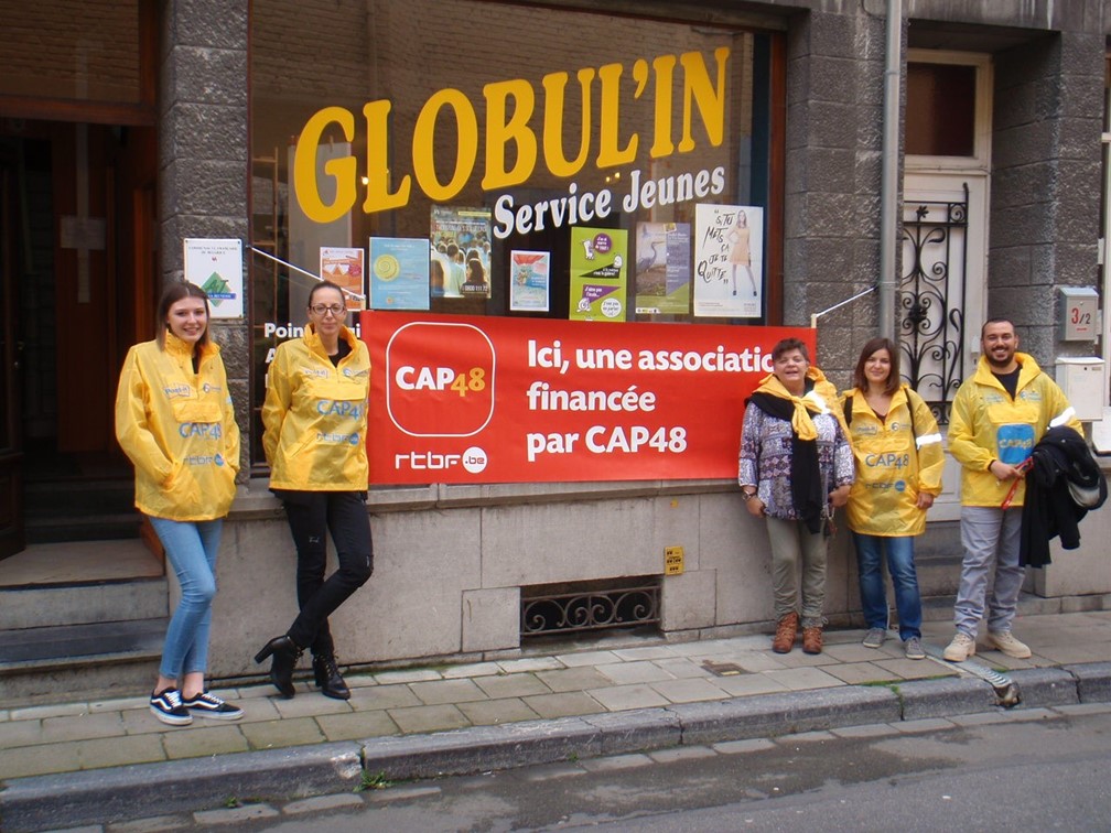Bénévoles posant devant l'entrée de Globul'in, service d'aide au jeunes en milieu ouvert (AMO), une asbl financée par CAP48