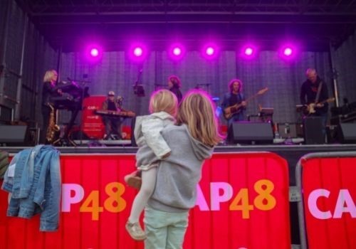 Vue de dos d'une jeune fille avec une enfant dans ses bras, toutes deux assistant à un concert solidaire organisé au profit de l'association CAP48